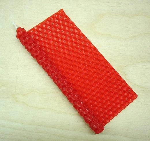 Kuvassa on punainen mehiläisvahalevy, jota on aloitettu rullaamaan kynttiläksi. Sydänlanka pilkistää rullan päästä.